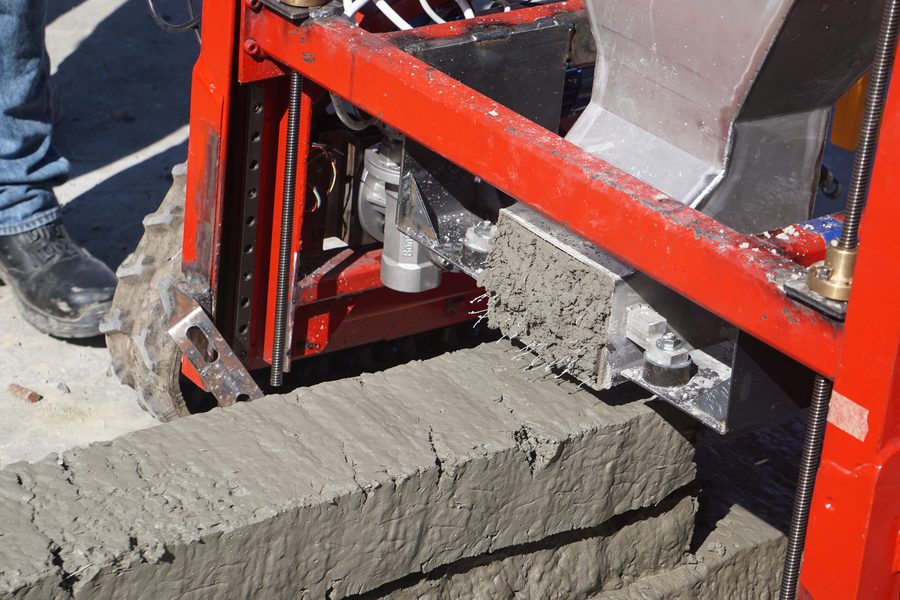 Close-up of the printer head shaping a fresh concrete wall section, layer by layer.
